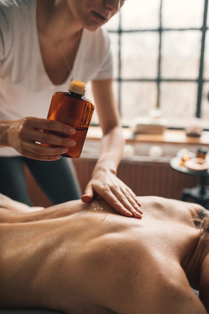 Oil poured from a bottle during a massage, in warm window light